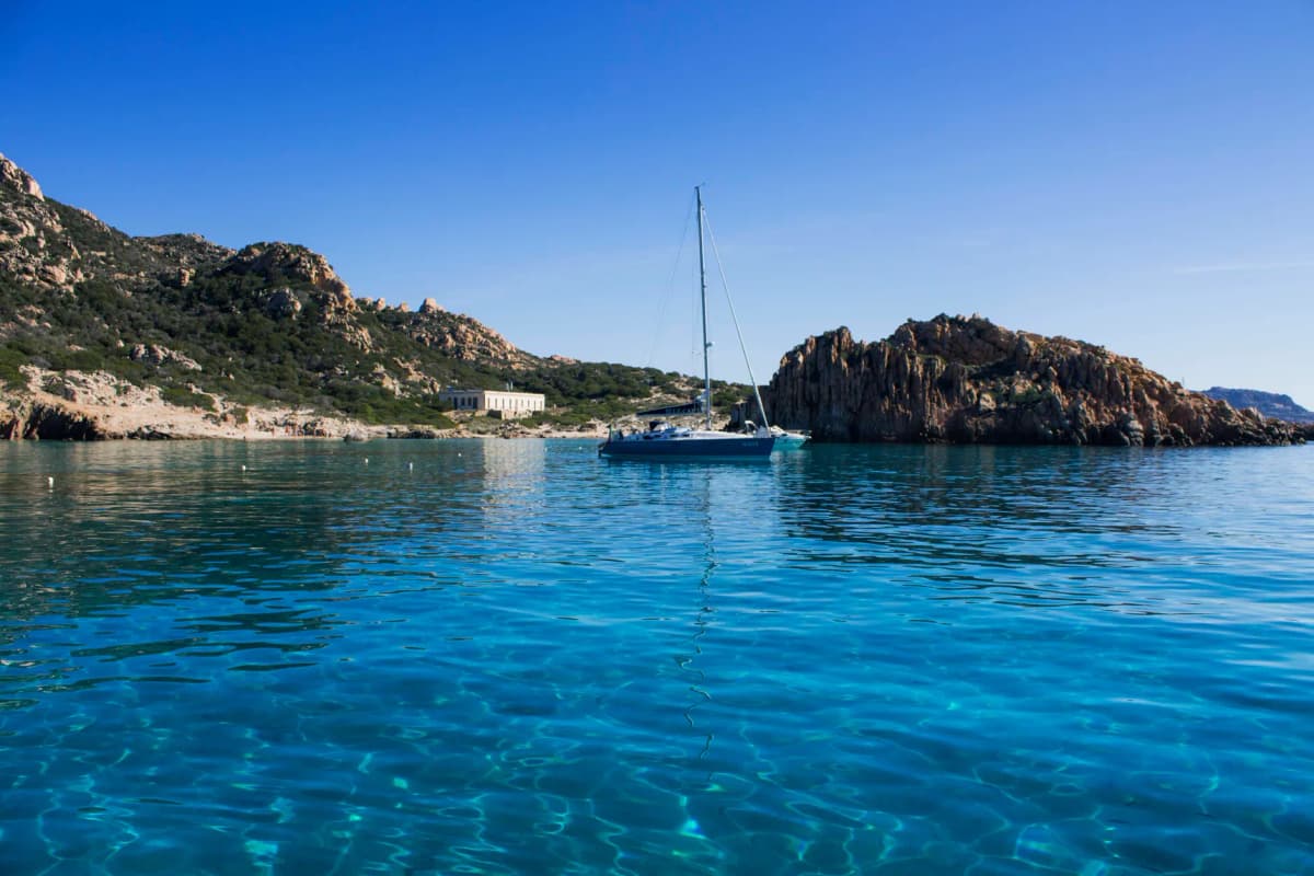 A sailboat floats tranquil in the clear blue waters of La Maddalena, Italy.