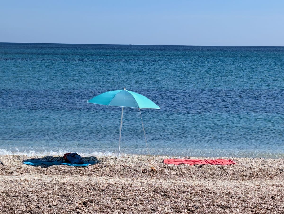 Plage abritée de Sardaigne, parasol et serviettes au bord de l'eau